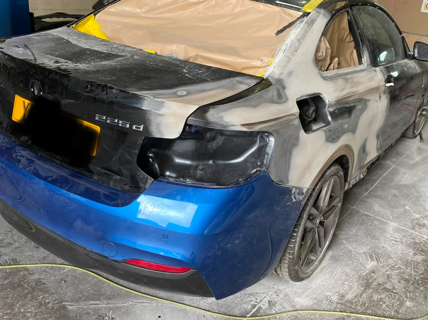BMW 2 Series in the workshop mid-repair, masked up with the rear quarter sanded back to primer